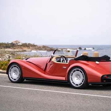 Red vintage convertible car parked along a coastal road with ocean views and wildflowers in the foreground.